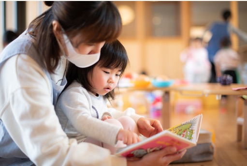 先生のひざの上で絵本を読む子ども